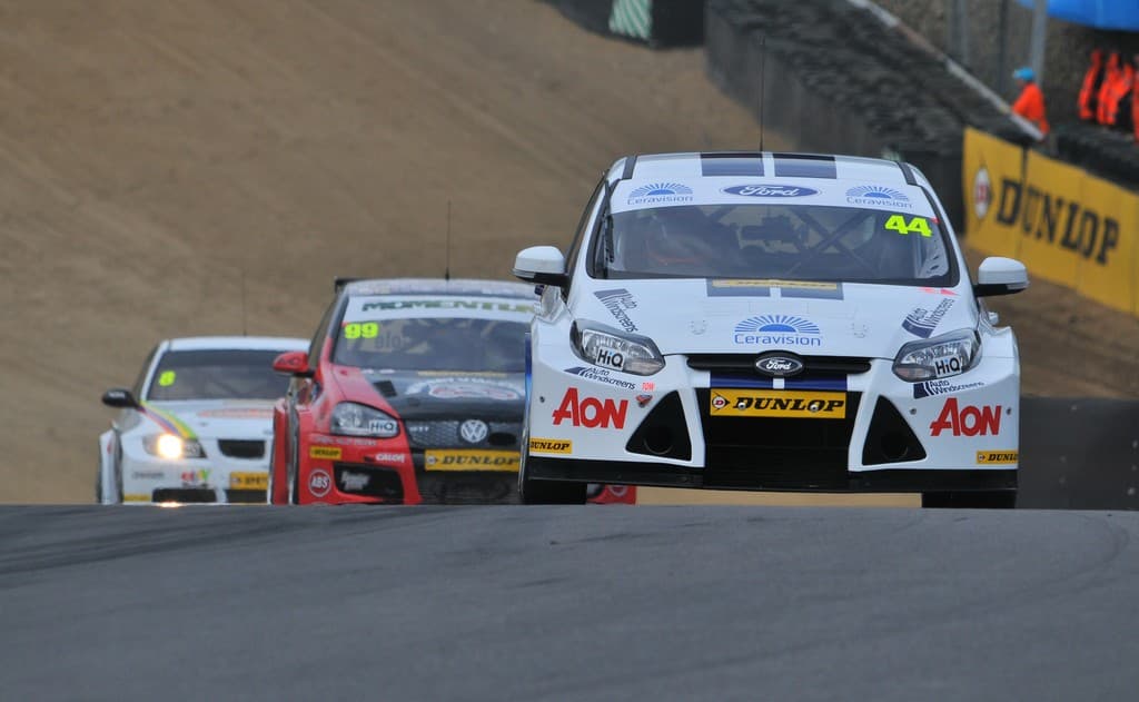 Touring cars racing on a circuit, with Aon branding visible on the lead car